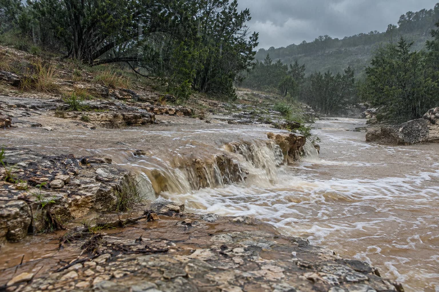 Rain runoff sheeting across thin soil and limestone ledges into a creek in the Texas Hill Country